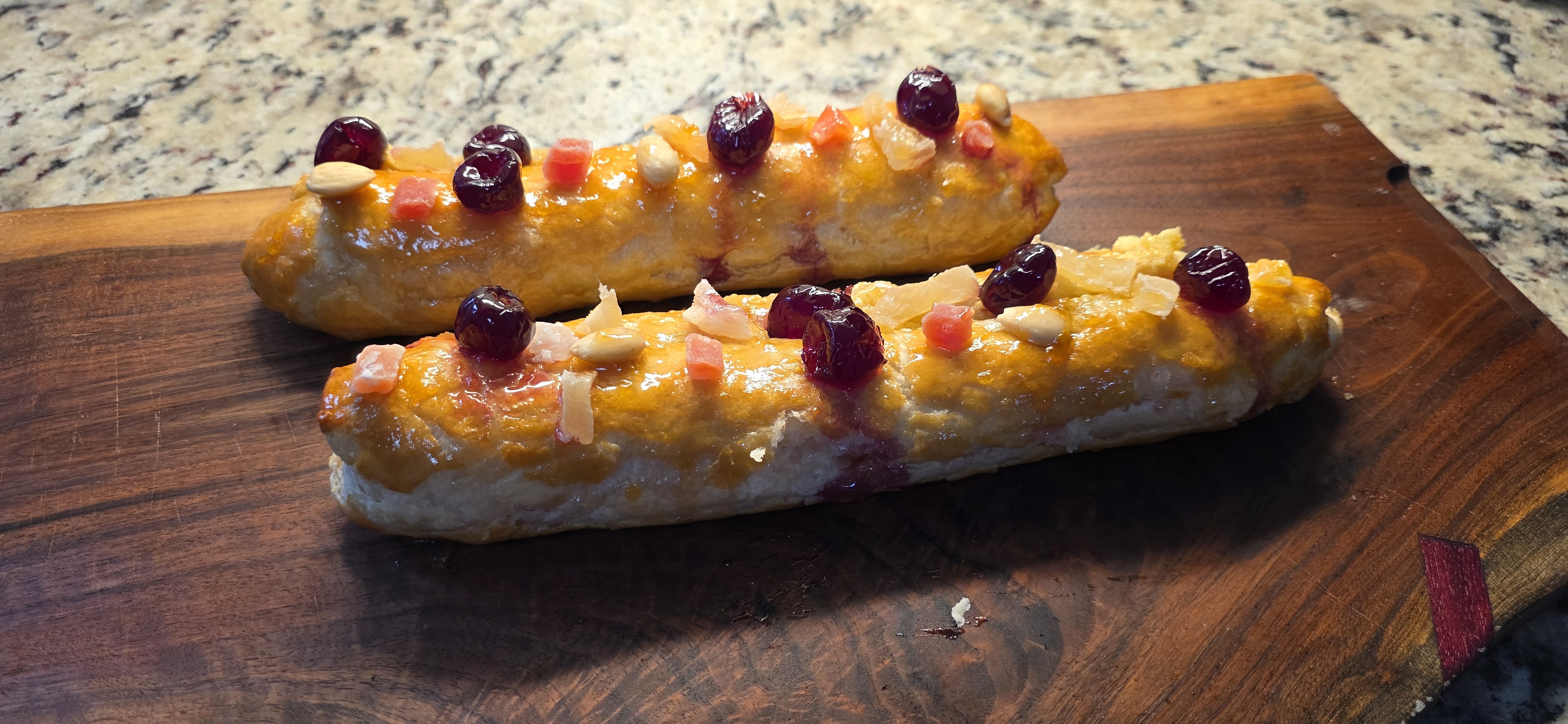 Two glazed banketstaaf pastries decorated with fruit and almonds